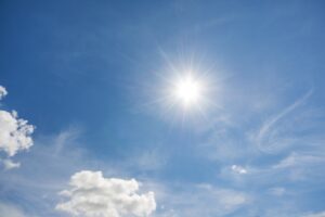 Sol på blå himmel med små vita moln