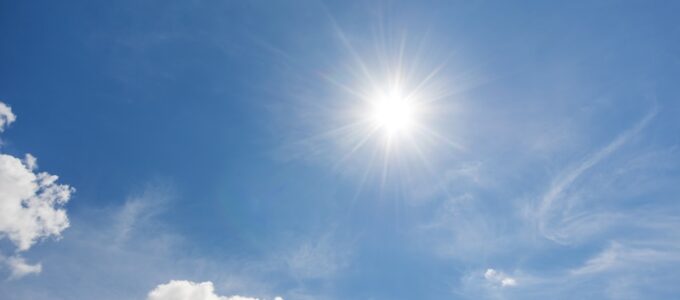 Sol på blå himmel med små vita moln